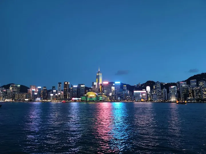 City skyline across body of water during night time The typical and iconic night scenery of the harbor front of Wanchai on H.K.Island, with Central Plaza (the t