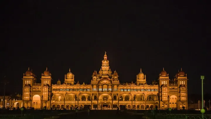 Mysore Palace illuminated with warm golden lights against a dark night sky: Mysore holiday packages by OYG Holidays