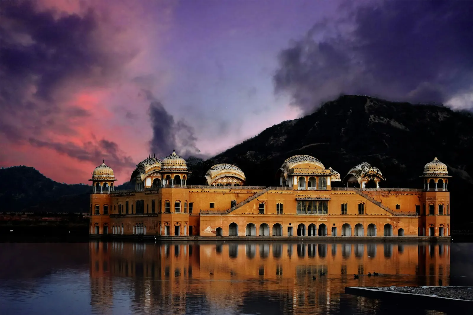Orange wall paint building near on mountain and body of water photo Jal Mahal: A timeless beauty surrounded by water and history: Rajasthan holiday packages by