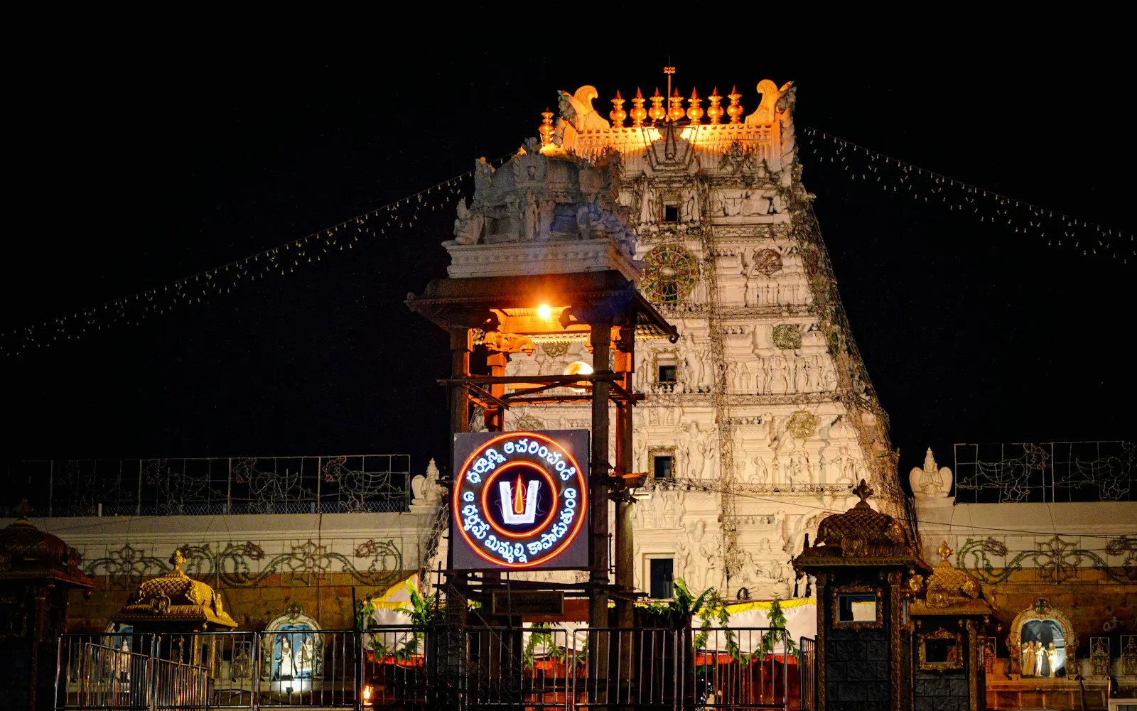 The illuminated gopuram of the Tirumala Venkateswara Temple at night in Tirupati A vibrant night view of a famous Indian temple with a glowing entrance, festive