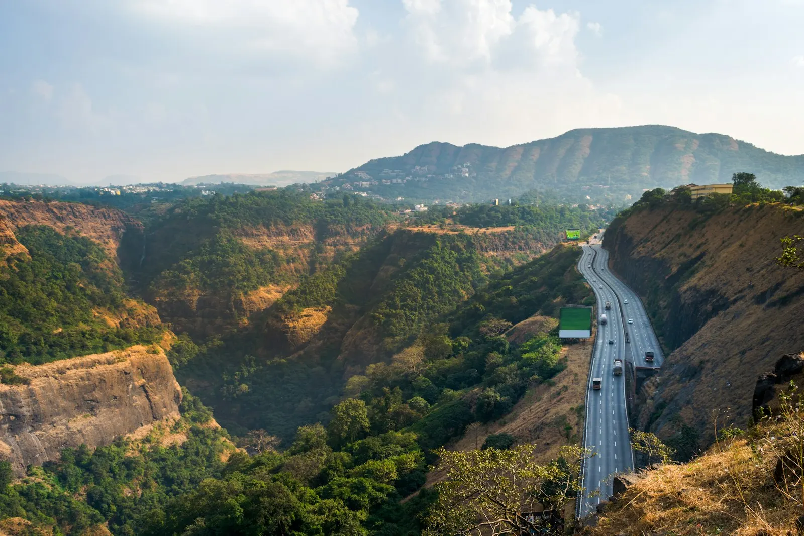 Cars on road between green trees under white cloudy sky during daytime Beautiful highway among the hills and valleys as viewed from Rajmachi Garden in Khandala